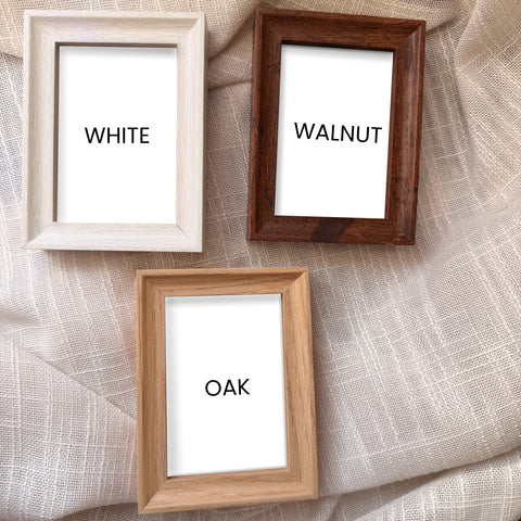 Three wooden picture frames labeled 'White', 'Walnut', and 'Oak' on a textured fabric background.